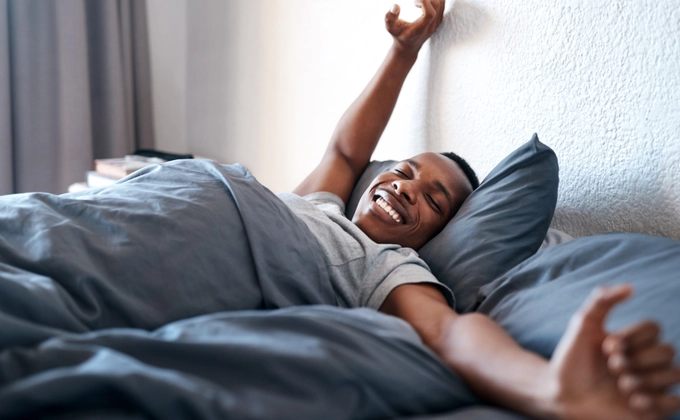 A man stretching in bed with a vibrant smile after a waking up in the morning
