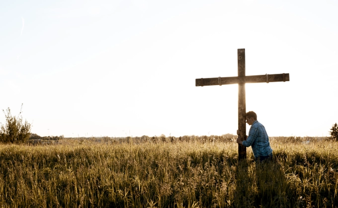 A man in a grassy field clinging to a cross