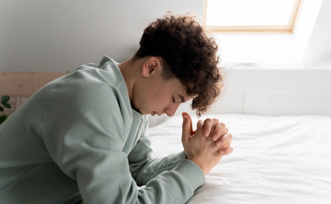 man kneeling and praying on bed
