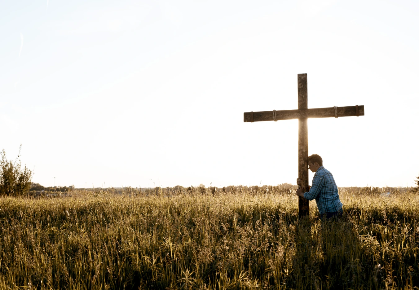 A man in a grassy field clinging to a cross