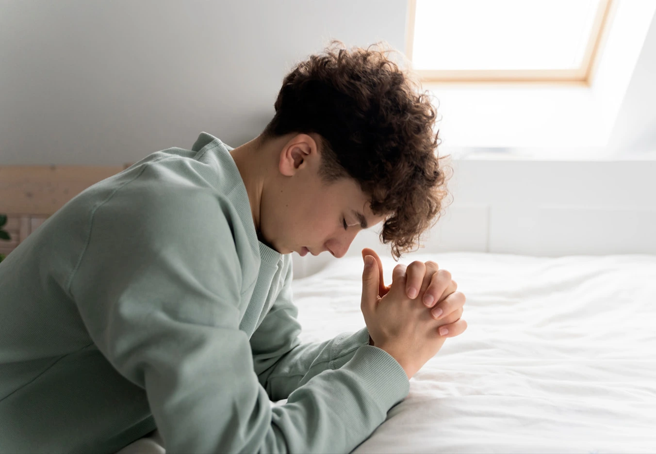 man kneeling and praying on bed