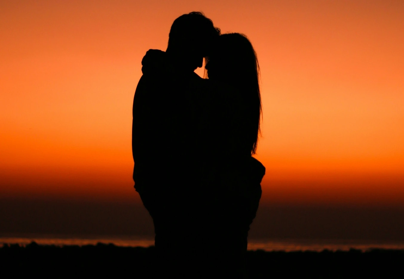 A Silhouette of two lovers hugging at sunset